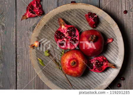 Ripe pomegranates whole and open in a ceramic gray plate on a gray wooden background Ripe pomegranates whole and open in a ceramic gray plate on a gray wooden background 119201285