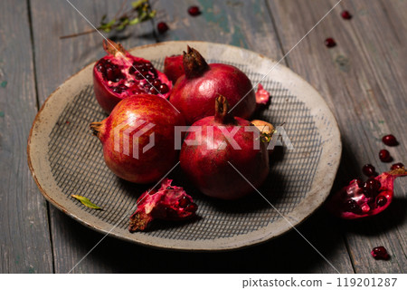 Ripe juicy pomegranates whole and open in a ceramic gray plate on a gray background Ripe juicy pomegranates whole and open in a ceramic gray plate on a gray background 119201287
