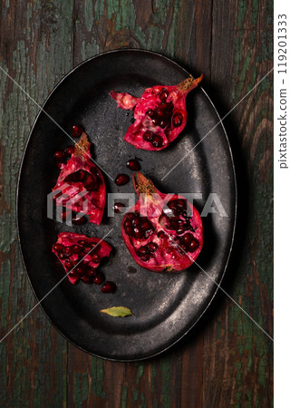 Open pomegranate fruit in a black metal tray on a wooden background Open pomegranate fruit in a black metal tray on a wooden background 119201333