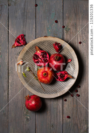 Ripe juicy pomegranates whole and open in a ceramic gray plate on a wooden background Ripe juicy pomegranates whole and open in a ceramic gray plate on a wooden background 119201336