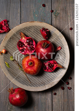 Pomegranates whole and open in a ceramic gray plate on a gray wooden background Pomegranates whole and open in a ceramic gray plate on a gray wooden background 119201337