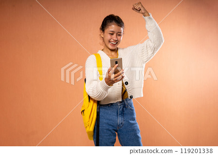 Joyful young woman celebrating with a smartphone and a yellow backpack Joyful young woman celebrating with a smartphone and a yellow backpack 119201338