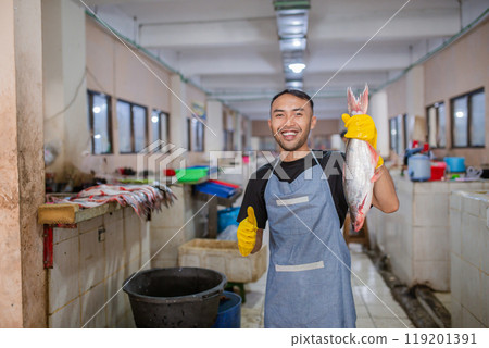 A Happy Fishmonger Smiling in the Fish Market While Holding the Fresh Catch 119201391