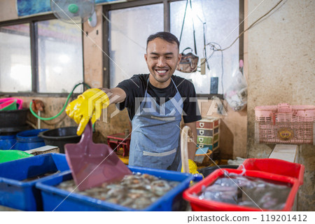 A cheerful fishmonger stands proudly at the market with a vibrant seafood selection 119201412