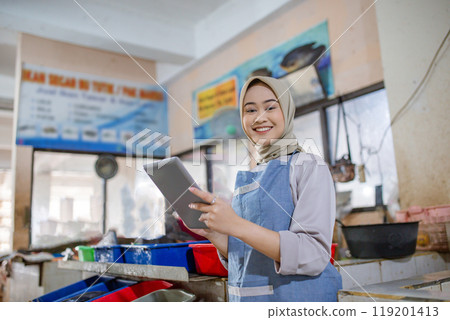 A Cheerful Smiling Woman Engaged with a Tablet in a Dynamic Food Business Environment A Cheerful Smiling Woman Engaged with a Tablet in a Dynamic Food Business Environment 119201413
