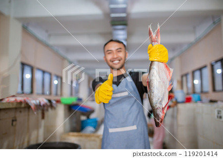 A Smiling Fishmonger Proudly Holding His Fresh Catch at a Bustling Market A Smiling Fishmonger Proudly Holding His Fresh Catch at a Bustling Market 119201414