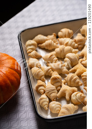 Small croissants and cookies in the shape of cats from puff pastry in a white baking dish, next to a pumpkin Small croissants and cookies in the shape of cats from puff pastry in a white baking dish, next to a pumpkin 119201490