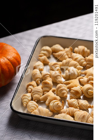 Small croissants and cookies in the shape of cats from puff pastry in a white baking dish, next to a pumpkin Small croissants and cookies in the shape of cats from puff pastry in a white baking dish, next to a pumpkin 119201491