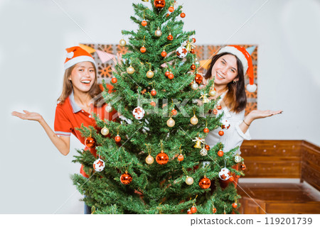 Joyful Friends Celebrating Christmas with a Beautiful Tree and Festive Hats Joyful Friends Celebrating Christmas with a Beautiful Tree and Festive Hats 119201739