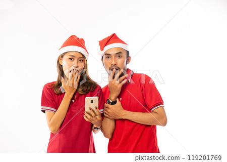 A Surprised Couple Wearing Santa Hats Joyfully Celebrating the Holiday Season Cheer A Surprised Couple Wearing Santa Hats Joyfully Celebrating the Holiday Season Cheer 119201769