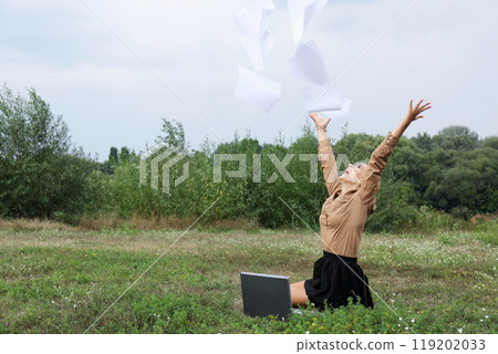 Woman in a field with a laptop open and papers flying around her 119202033