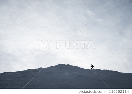 Silhouette shot of hiker approaching snowy mountain summit during winter 119202114