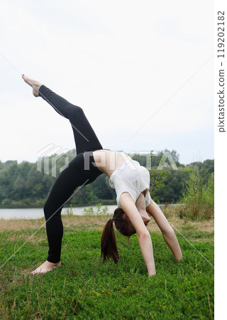A teenage girl is doing a handstand on the training ground near the river A teenage girl is doing a handstand on the training ground near the river 119202182