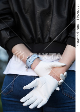 A woman in a brutal black leather jacket and white leather gloves. Photo from the back close-up A woman in a brutal black leather jacket and white leather gloves. Photo from the back close-up 119202279