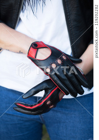 A woman in a black jacket wearing black driving gloves with red decorative seams, close-up A woman in a black jacket wearing black driving gloves with red decorative seams, close-up 119202282