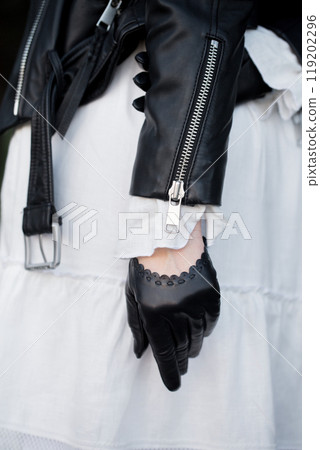 A woman in a vintage feminine dress, black brutal jacket and black gloves outdoors, close-up A woman in a vintage feminine dress, black brutal jacket and black gloves outdoors, close-up 119202296