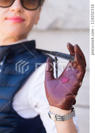 A woman in gloves and a whip in her hands is standing in a stable 119202318