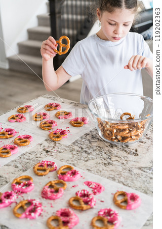 With focused attention, this budding culinary artist dips pretzels into a pot of melted chocolate, creating sweet delights in the warmth of a well-lit home kitchen. With focused attention, this budding culinary artist dips pretzels into a pot of melted chocolate, creating sweet delights in the warmth of a well-lit home kitchen. 119202363