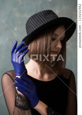 Pensive woman in black hat and blue leather gloves on gray background Pensive woman in black hat and blue leather gloves on gray background 119202462