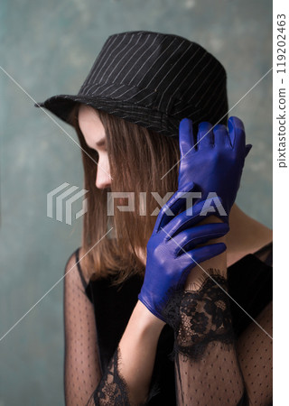 Young sad woman in black hat and blue leather gloves on gray background 119202463