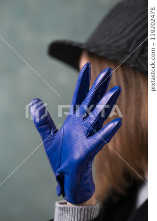 Pensive woman in blue leather gloves covers his face with his hands on gray background, hand close-up 119202478