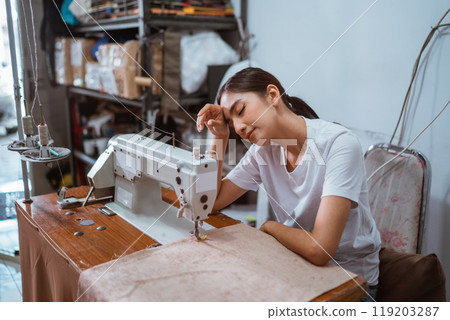 tired female tailor sweping her sweat while sewing the curtain 119203287