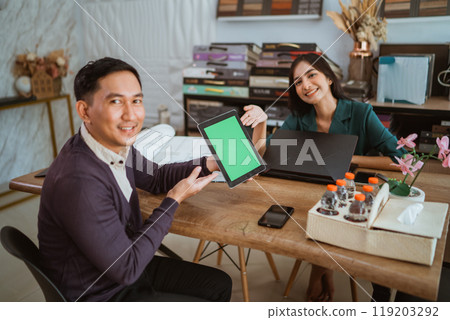 asian female shopkeeper smiling while pointing on the green screen digital tablet 119203292