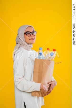 asian muslim woman posing sideways holding paper bag filled with plastic bottle asian muslim woman posing sideways holding paper bag filled with plastic bottle 119203374