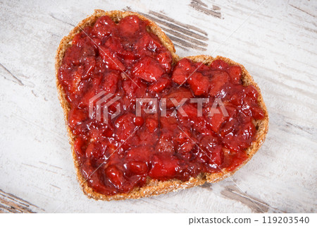 Bread in shape of heart with strawberry jam for breakfast. Rustic background 119203540