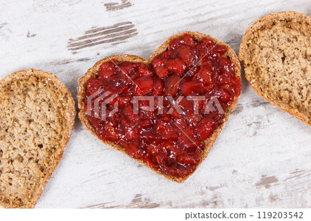 Slice of bread in shape of heart with strawberry jam for breakfast. Rustic background Slice of bread in shape of heart with strawberry jam for breakfast. Rustic background 119203542