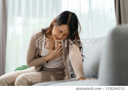 A woman is holding her hand on her chest. She is in pain and she is suffering from a heart attack 119204151
