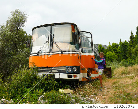 Vintage Orange Bus Abandoned in Nature with Explorer Nearby 119205072