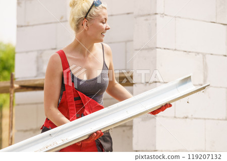 Woman carrying gutter on construction site 119207132