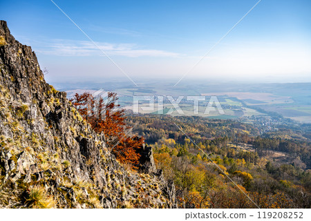 On a sunny autumn day, vibrant foliage contrasts against rocky outcrops on Sedlo Mountain, revealing a panoramic view of the Central Bohemian Uplands and surrounding valleys. On a sunny autumn day, vibrant foliage contrasts against rocky outcrops on Sedlo Mountain, revealing a panoramic view of the Central Bohemian Uplands and surrounding valleys. 119208252