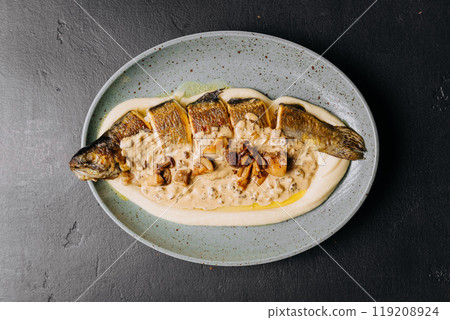 Whole roasted fish with creamy mushroom sauce and mashed potatoes on a ceramic plate 119208924