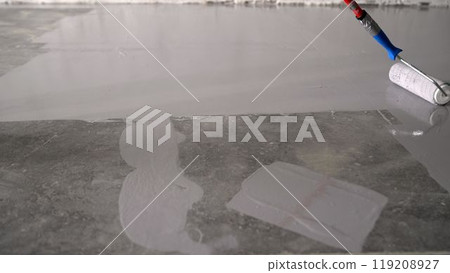 Construction worker applying epoxy coating on concrete floor using a roller. 119208927