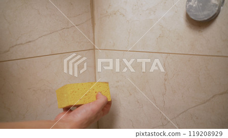 Construction worker cleaning the grout after applying it on a bathroom wall with a sponge 119208929