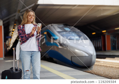 A young traveler is at a bustling train station, actively using their smartphone device A young traveler is at a bustling train station, actively using their smartphone device 119209384