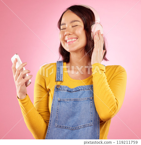 Woman, headphones and cellphone for smile, studio or thinking for sound, idea and relax by pink background. Happy gen z girl, Japanese student and music app for listening with streaming subscription 119211759