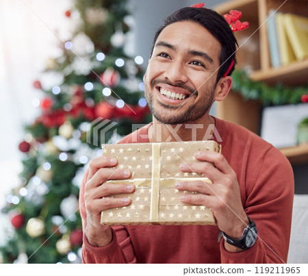 Christmas, smile and asian man with gift in his home happy, excited and having fun holiday celebration. Hand holding, box and Japanese male with present in a living room at December party or event 119211965