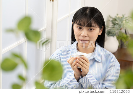 Woman standing by the window with a coffee cup Woman standing by the window with a coffee cup 119212063