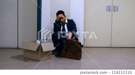 Businessman, fired and stress with box at workplace with unemployment, failure and disappointment on floor. Professional, employee and helpless in corridor of office building with bag, leaving or sad Businessman, fired and stress with box at workplace with unemployment, failure and disappointment on floor. Professional, employee and helpless in corridor of office building with bag, leaving or sad 119212310