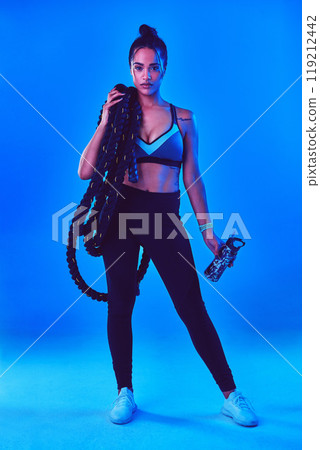 It never gets easier, you just get stronger. Full length shot of an attractive young sportswoman posing carrying battle ropes against a blue background. 119212442