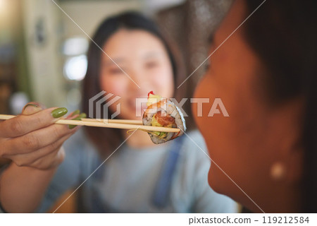 Chopsticks, restaurant feeding and friends hands with sushi and Asian cuisine eating at cafe. Happy, hungry women and plate of food at Japanese bar with friendship, smile and bonding from table meal 119212584