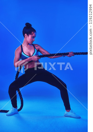 You wont know your limits until you push yourself. Full length shot of an attractive young sportswoman working out with battle ropes against a blue background. 119212994