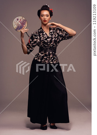 Fashion, fan and Japanese woman with geisha and Asian clothing with traditional outfit in studio. Culture, creative and ancient heritage clothes with female person from Japan with brown background Fashion, fan and Japanese woman with geisha and Asian clothing with traditional outfit in studio. Culture, creative and ancient heritage clothes with female person from Japan with brown background 119213109