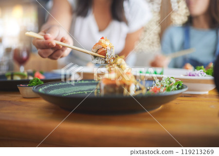 Sushi, hand and eating food with chopsticks at a restaurant for nutrition and health. Closeup of a hungry people with wooden sticks for dining, Japanese culture and cuisine with creativity on plate 119213269