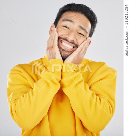 Smile, shy and hands on face of asian man in studio for in love, sweet or gesture on grey background. Happy, portrait and Japanese male model pose with emoji cheeks expression for romantic sign 119213284