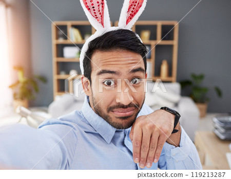 Bunny ears, holiday and selfie with a man and remote work on easter with creative job. Celebration, happy and male professional from Spain feeling silly and goofy with comedy rabbit hat in a home 119213287