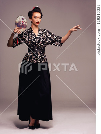 Fashion, dance and Japanese woman with geisha fan and Asian clothing with traditional outfit in studio. Culture, creative and heritage clothes with female person from Japan with brown background 119213322
